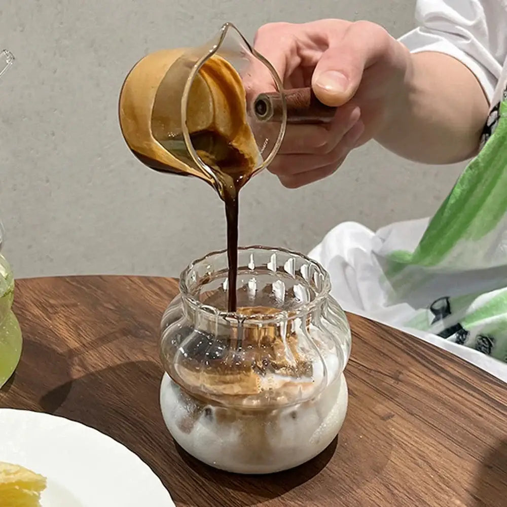 A clear glass pitcher pouring dark coffee into a ribbed cocktail glass from the 650ml latte ribbed glass set