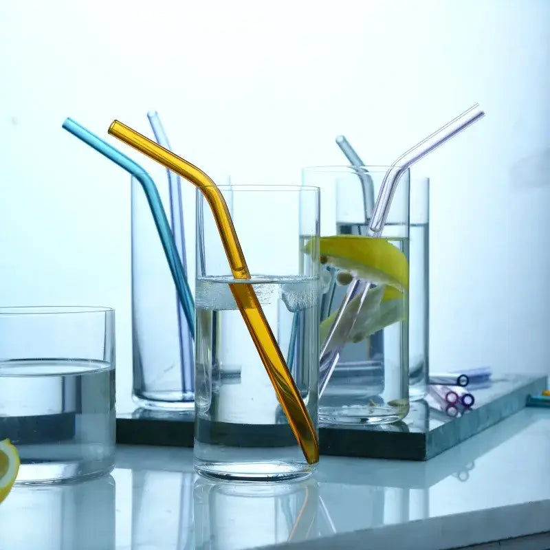 A golden-tinted curved juice straw from decorbites heat-resistant glass straws in a glass with lemon water