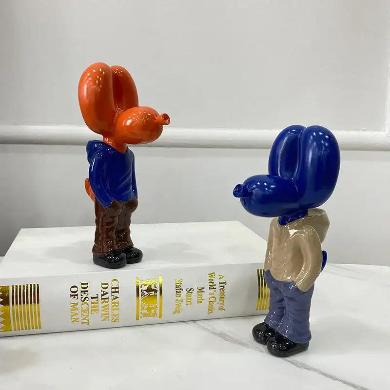 Two glossy resin balloon dog statues in orange blue and deep blue beige on a white book for home decor