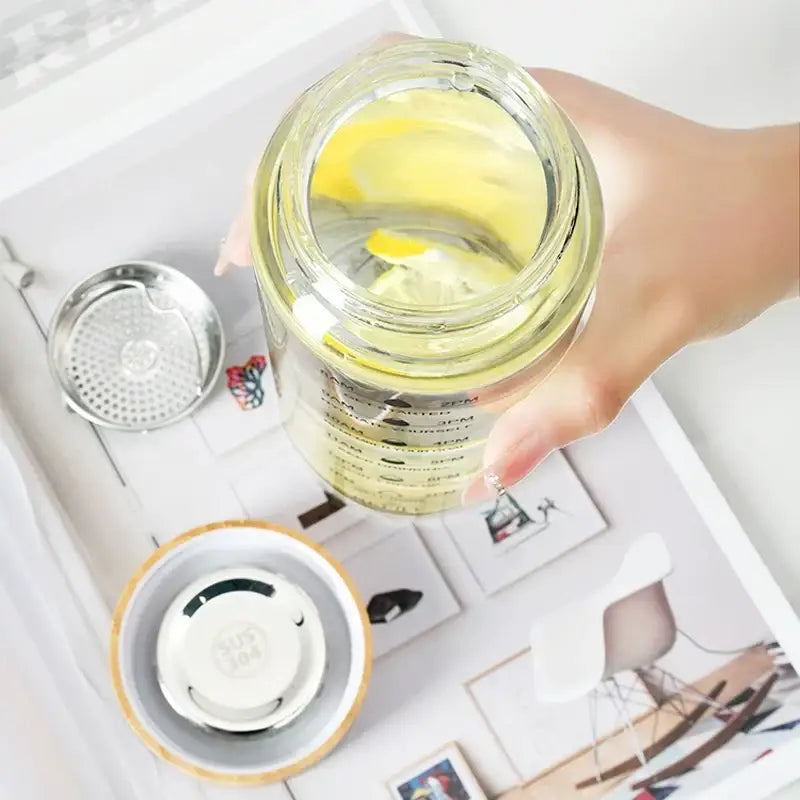 Decorbites™ 700ml glass water bottle with bamboo lid and silver tea filter filled with yellow liquid