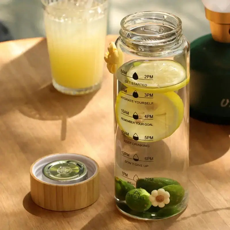 Decorbites™ 700ml glass water bottle with bamboo lid, yellow lemon accents, and hourly hydration reminders in black text