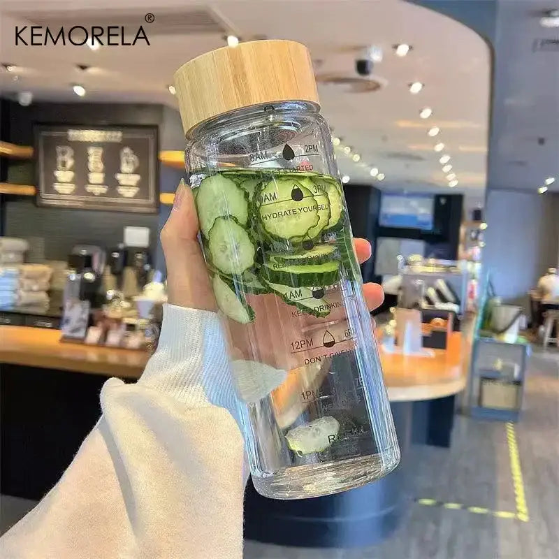 DecorBites™ 700ml clear glass water bottle with bamboo lid, time scale, and stainless steel tea filter filled with cucumbers