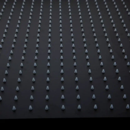 Rows of uniform white plastic spikes embedded in a black ultra-thin rain shower head surface for bathroom use