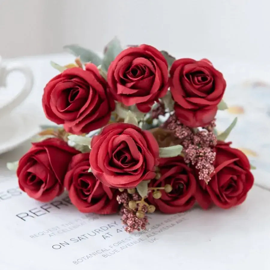 A bouquet of vibrant red artificial roses with green leaves and pink embellishments in a pink peony silk bouquet design