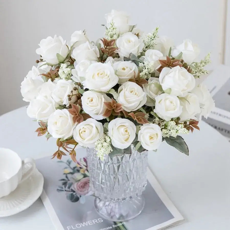 A clear faceted crystal vase with white artificial roses and brown leaves complementing the pink peony silk bouquet