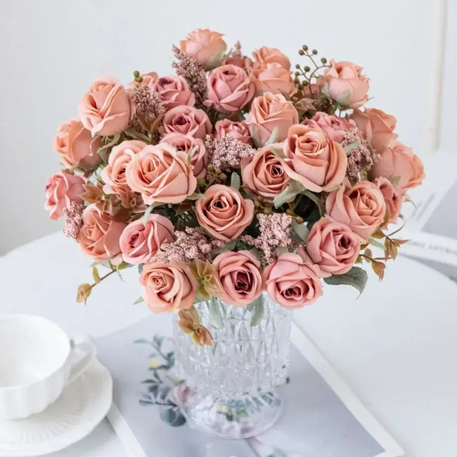 A peony silk bouquet of soft peach-colored roses and delicate greenery in a clear faceted crystal vase for decoration