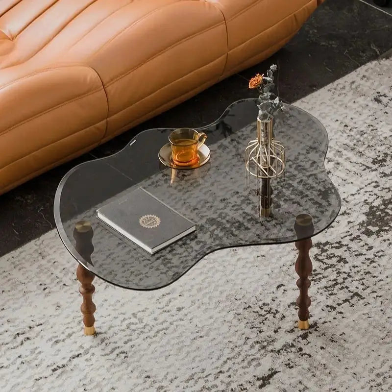 A sleek dark-tinted glass solid wood coffee table with a peanut shape and ornate legs for living room decor