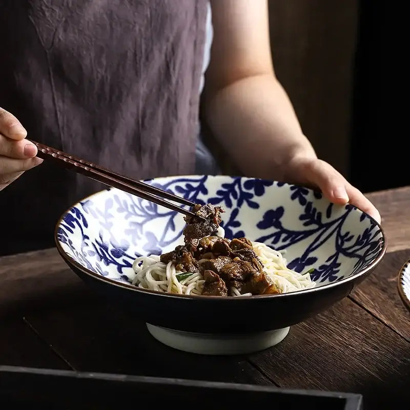 A ceramic japanese ramen bowl with black exterior and blue floral interior filled with noodles and meat soup