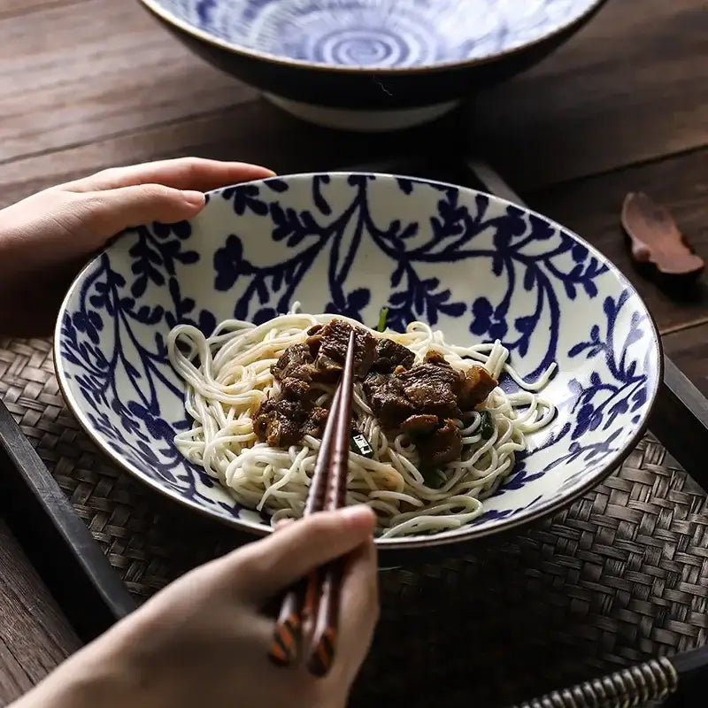 Blue and white ceramic japanese ramen bowl with intricate floral patterns holding noodles and meat for soup or salad