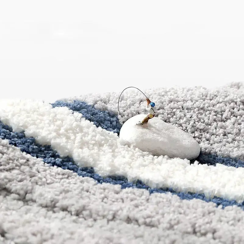 A miniature fishing figurine on a smooth white stone on a soft blue and white striped decorbites absorbent water bathroom mat