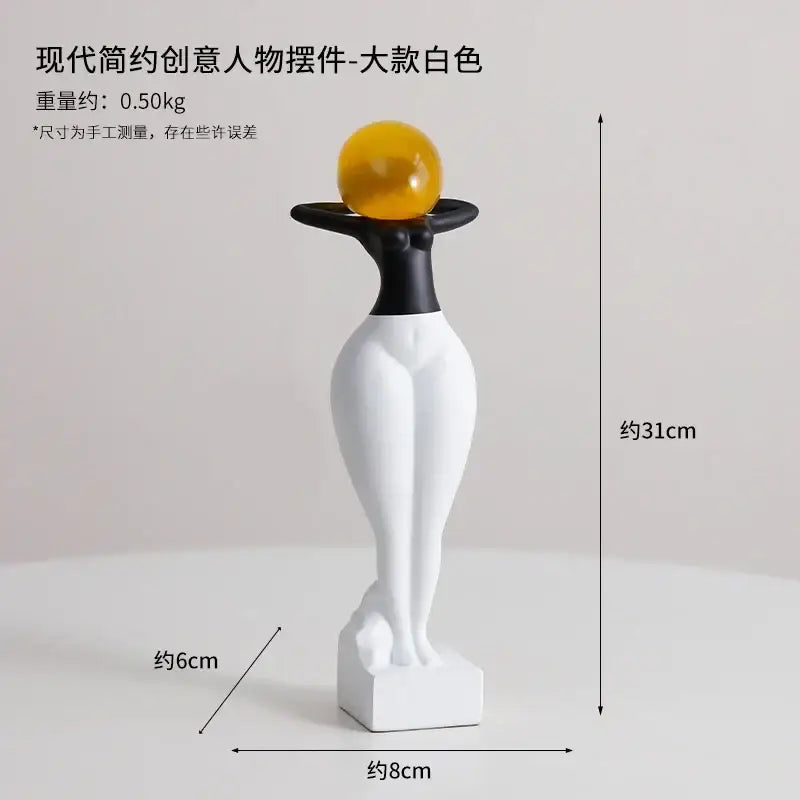 A sleek black and white resin decorbites abstract art female figurine balancing an amber glass sphere on her head