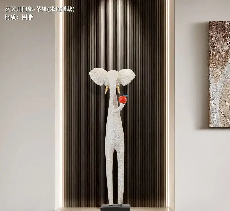 A sleek white resin elephant sculpture with gold tusks holding a red apple in decorbites abstract art living room decor