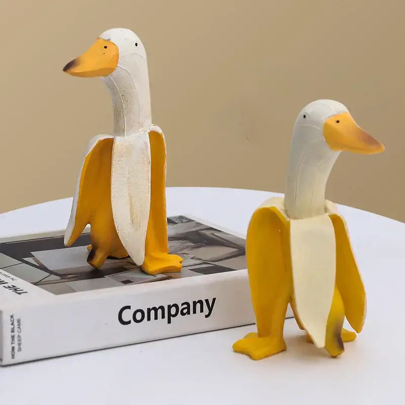 Two whimsical white and yellow decorative figurines designed as abstract banana duck sculptures for home decoration