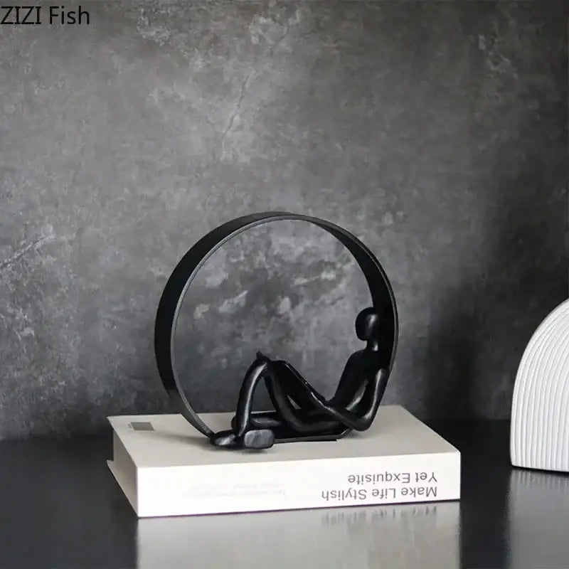 DecorBites™ abstract black characters resin sculpture of a seated figure inside a circular frame on a white book