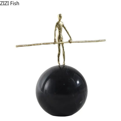 Gold-toned abstract character marble sculpture balancing on rod atop glossy black base for marble sculpture room decor