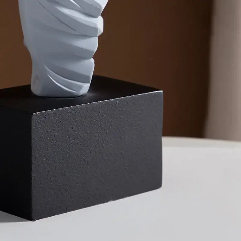A sleek light gray twisted ceramic decorbites abstract dancer figure on a textured black square base for modern decor