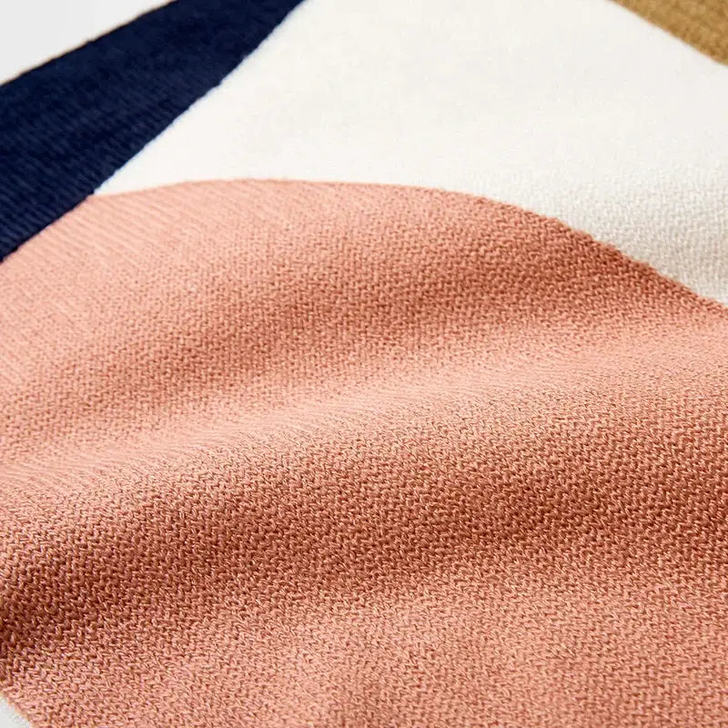 A soft peach knitted sweater with navy cream stripes shown alongside decorbites abstract embroidered pillow cover