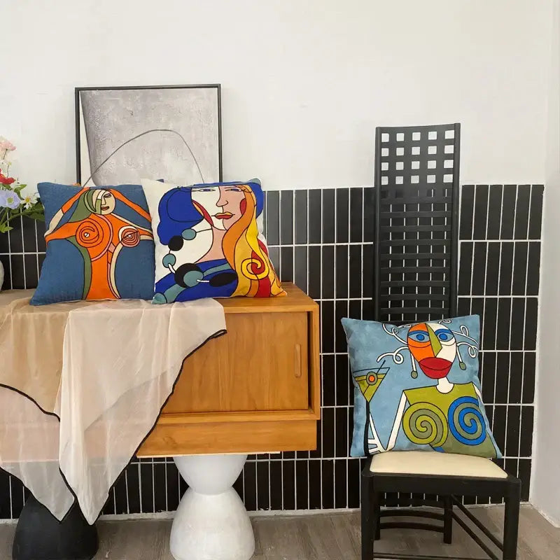 Three colorful decorbites abstract embroidery pillowcases 45x45cm with stylized faces on wooden cabinet and chair