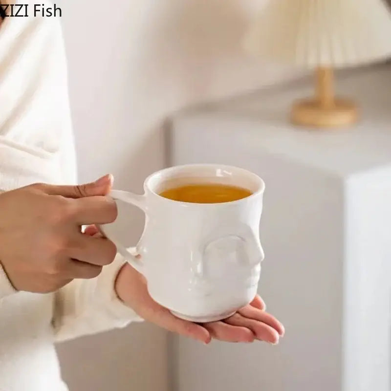 White ceramic decorbites abstract face ceramic mug with embossed features filled with golden tea for coffee or tea