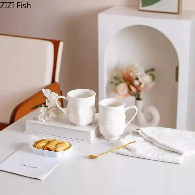 Two white decorbites abstract face ceramic mugs with textured sculpted surfaces on stacked books for dining use
