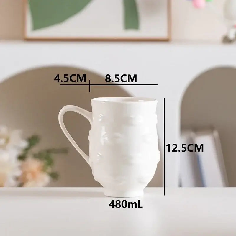 White ceramic DecorBites™ abstract face ceramic mug with textured embossed design and sturdy handle for coffee and tea