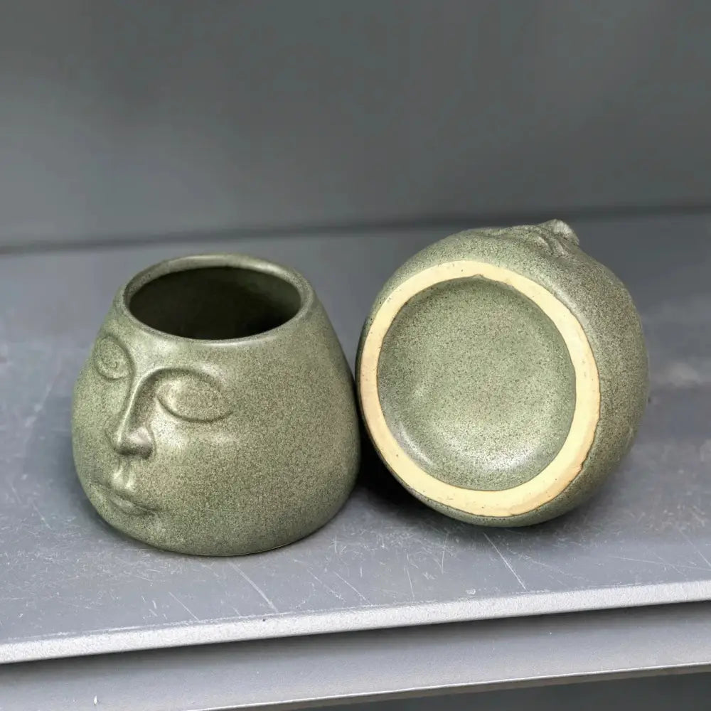 A matte sage green abstract face ceramic planter with closed eyes by decorbites for home decor accessories