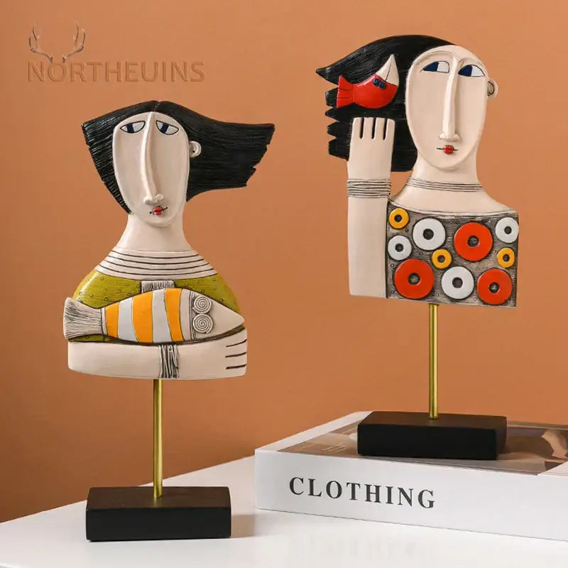 Two stylized black hair ceramic figurines with fish and circular patterns in DecorBites abstract face resin art statues