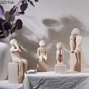 Four minimalist ceramic figurines depicting children in seated poses on square bases from decorbites abstract family character sculpture