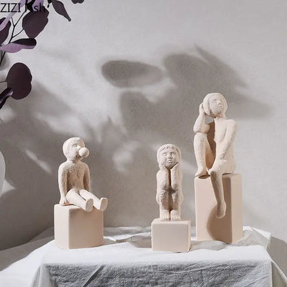 Three minimalist beige ceramic children figurines seated on square pedestals decorbites abstract family character sculpture