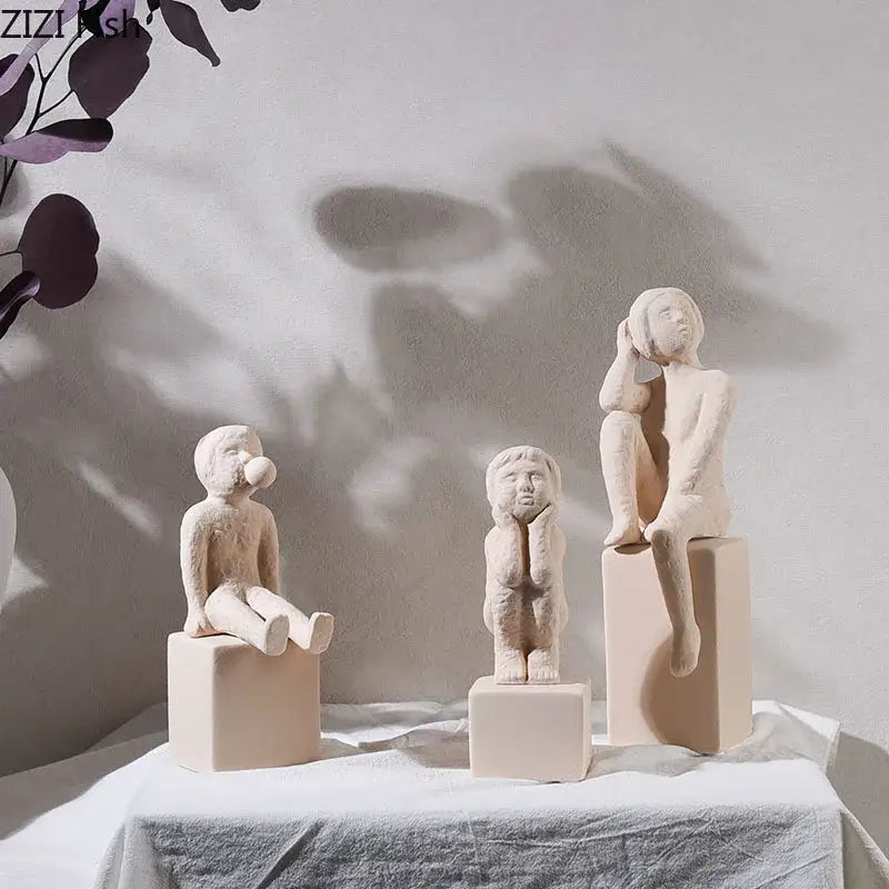 Three minimalist beige ceramic children figurines seated on square pedestals decorbites abstract family character sculpture