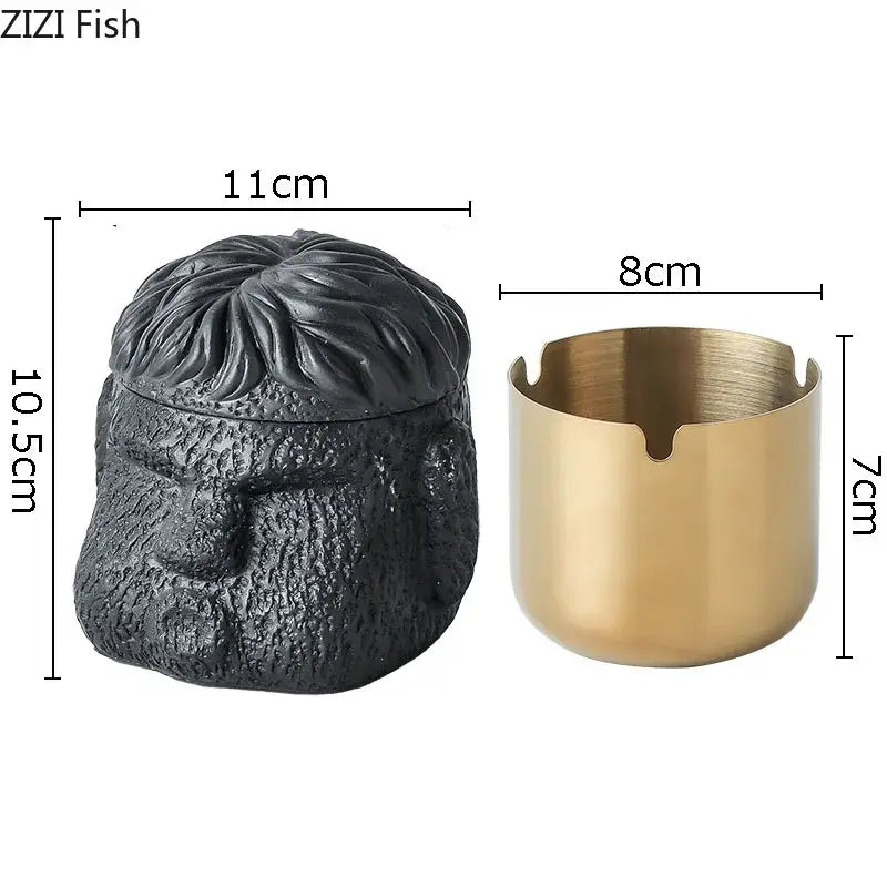 Black textured skull-shaped portraits cement ashtray with gold-toned cylindrical base and four notches for smoking accessories