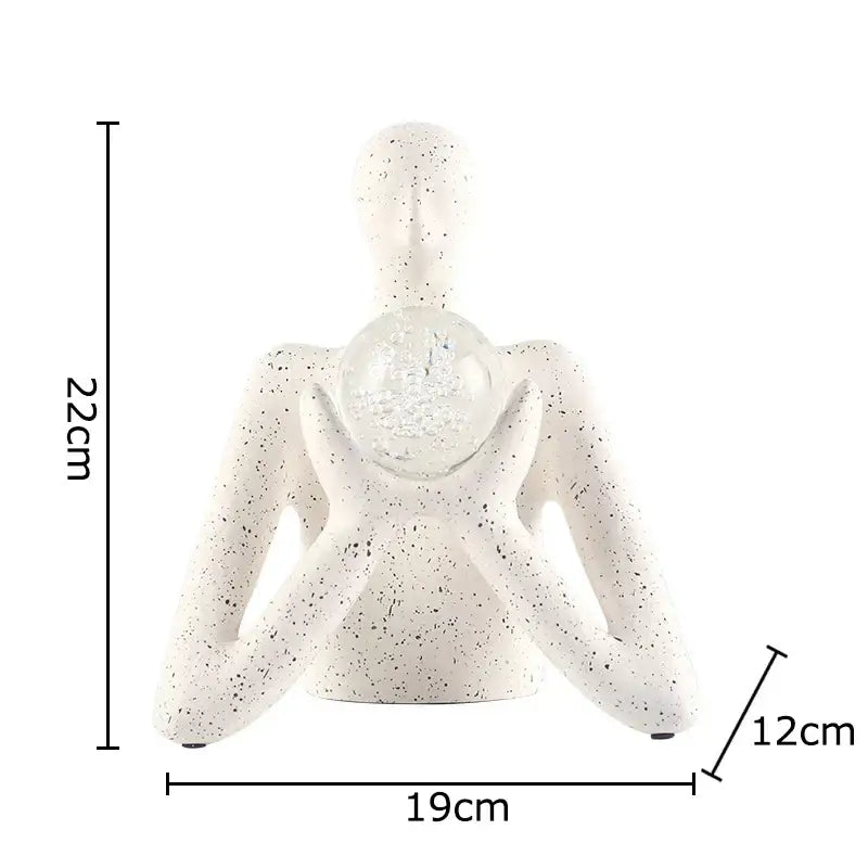 White speckled resin sculpture decor of a seated human holding a clear glass orb from DecorBites abstract figures collection