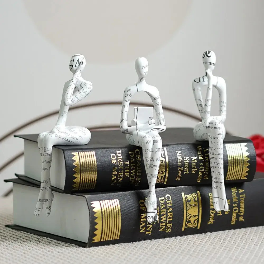Three white paper-textured decorbites abstract figurine modern sculptures seated on stacked black books for home decor
