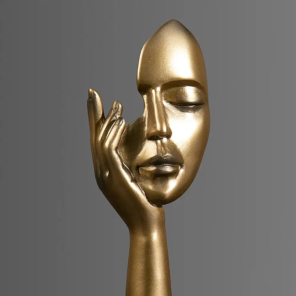 Golden metallic decorbites abstract figurines sculpture of a face with closed eyes cradled by an outstretched hand