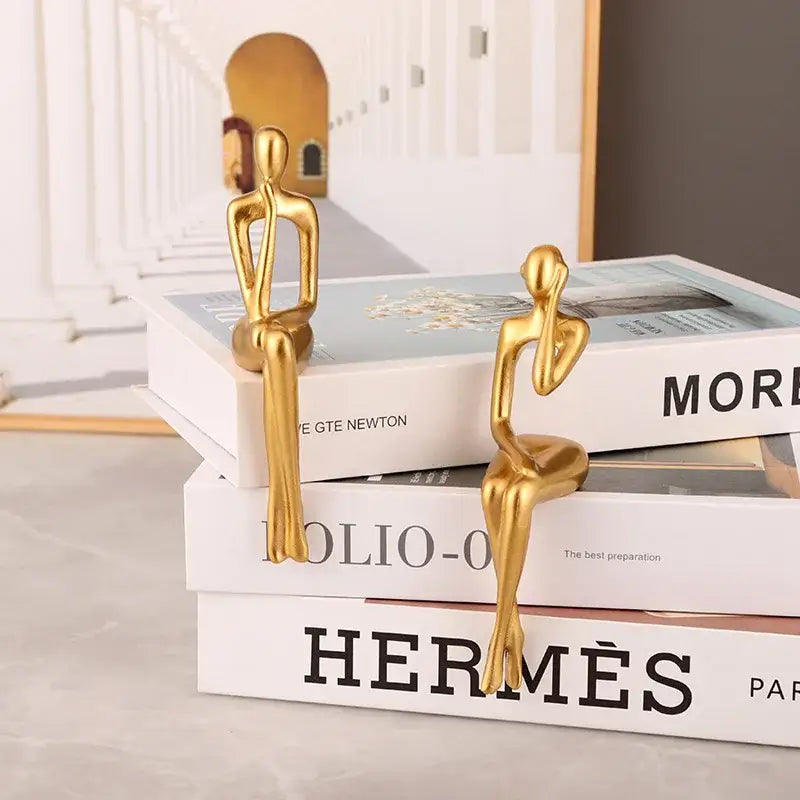 Two sleek gold-colored minimalist abstract figurines sit atop stacked books in the decorbites abstract figurines set