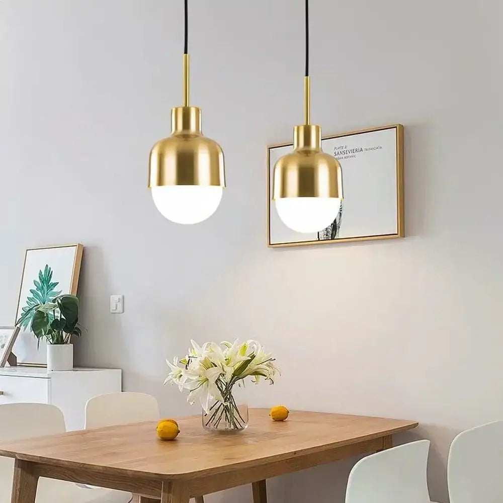 Two gold-finished acrylic ball pendant lights with rounded glass shades hang above a wooden dining table decorbites pendant light