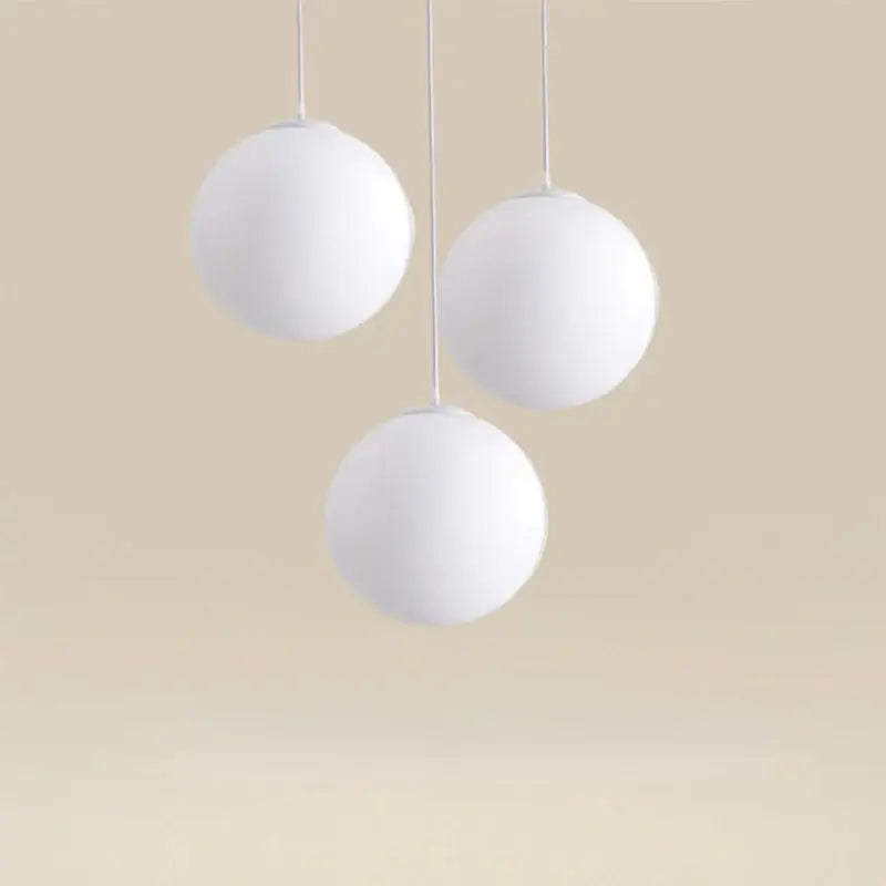 Three white acrylic ball pendant lights hang from thin cords in a modern Nordic style for living room decor