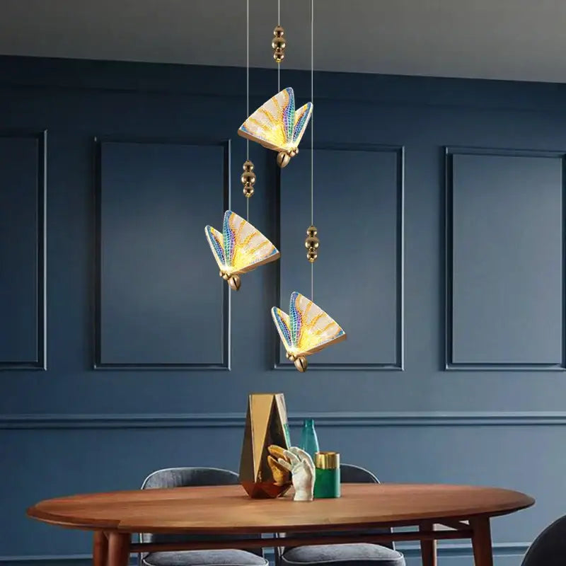 Three golden acrylic butterfly chandelier ceiling lamps with iridescent blue and yellow wings in a modern dining room