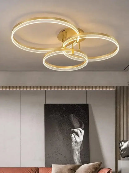 Gold-toned acrylic ceiling chandelier with three interlocking circular rings emitting warm glow for modern living rooms