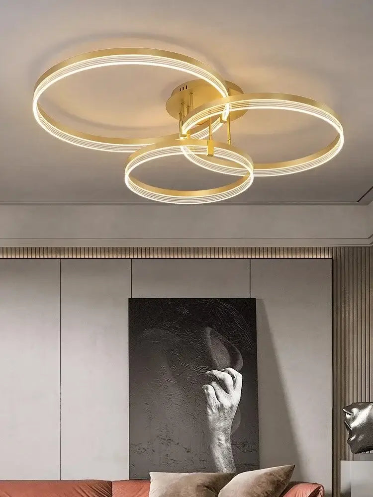 Gold-toned acrylic ceiling chandelier with three interlocking circular rings emitting warm glow for modern living rooms