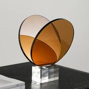 A modern amber acrylic crystal bookshelf magazine rack featuring two overlapping translucent glass discs with black rims mounted on a clear base