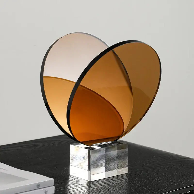 A modern amber acrylic crystal bookshelf magazine rack featuring two overlapping translucent glass discs with black rims mounted on a clear base