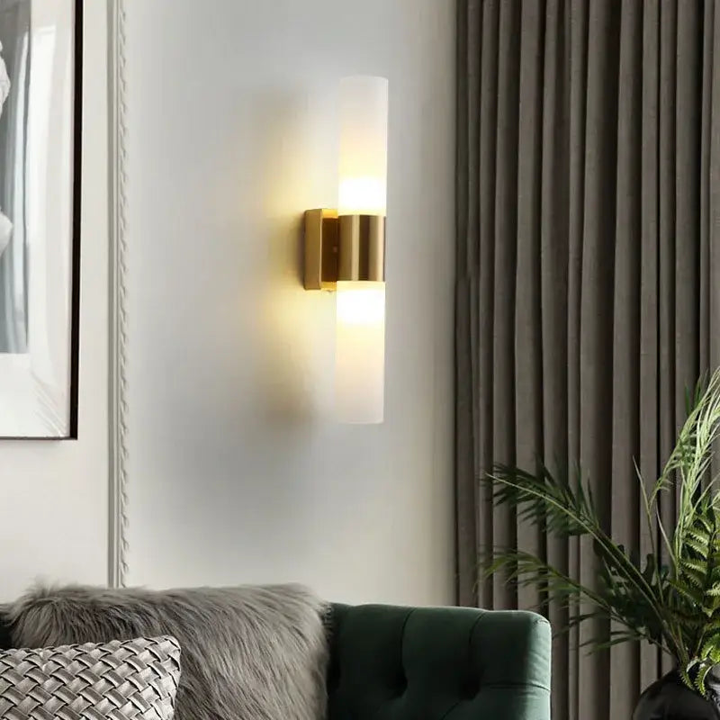 Modern gold-toned decorbites™ acrylic cylinder wall lamp with frosted glass diffuser emitting warm light for bedroom and living room