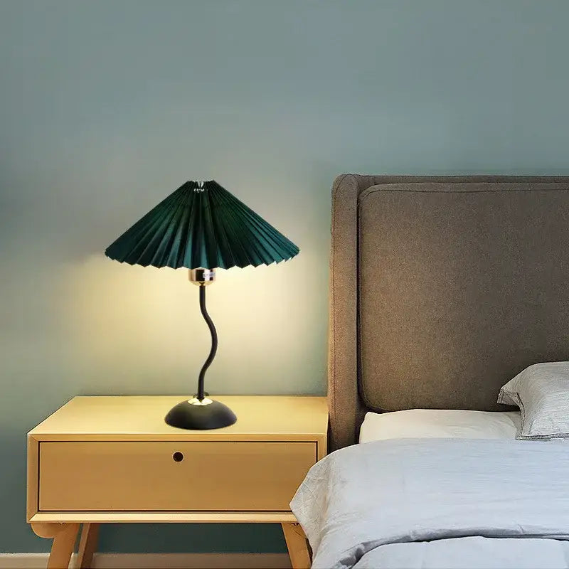 Decorbites adjustable pleated table lamp with dark green fabric shade, curved black base, and metallic stem on wooden nightstand