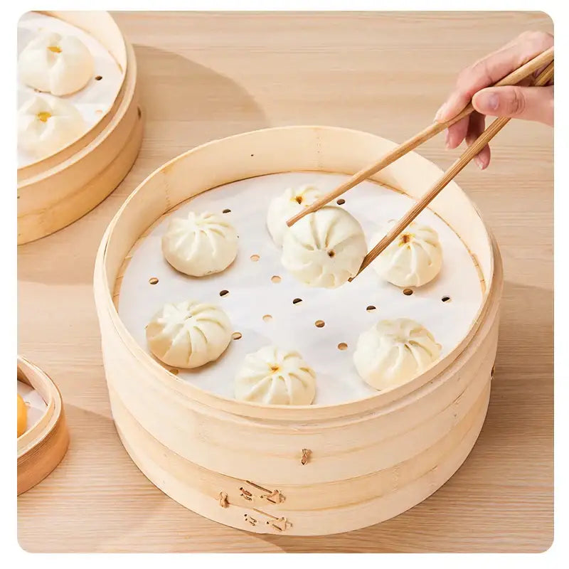 A round bamboo steamer basket with white perforated decorbites™ air fryer steamer papers holding pleated dumplings
