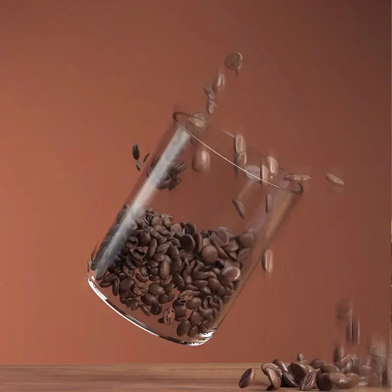 A clear glass coffee bean storage jar filled with dark roasted beans and bamboo lid for airtight kitchen preservation