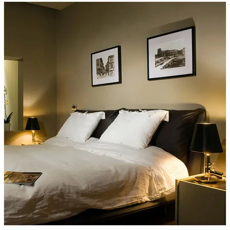 A plush black upholstered bed with white pillows and duvet next to a decorbites ak47 gun design table lamp