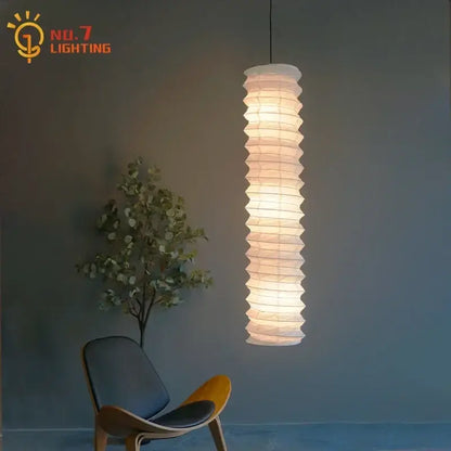 A tall white rice paper pendant light with accordion pleats and warm glow from the DecorBites akari noguchi pendant