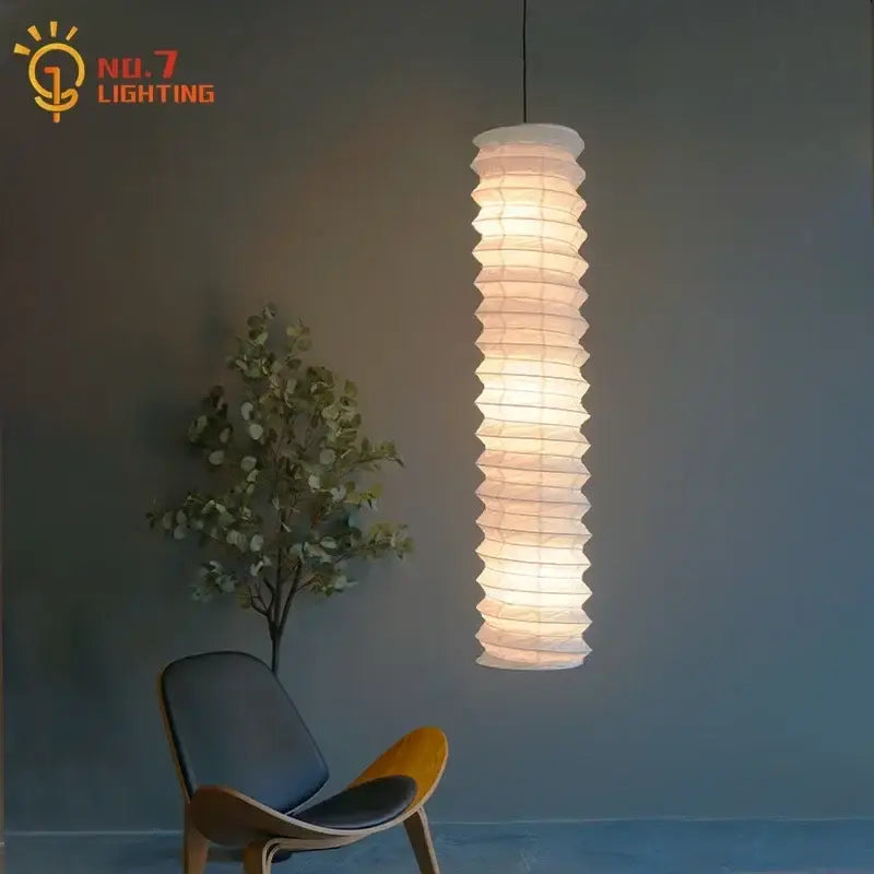 A tall white rice paper pendant light with accordion pleats and warm glow from the DecorBites akari noguchi pendant