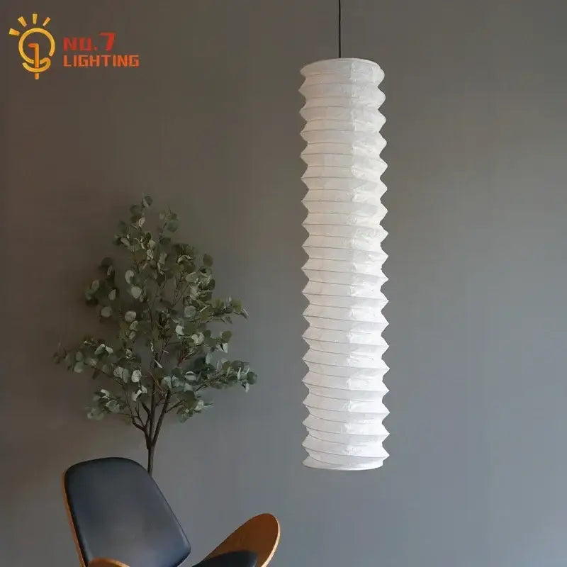 A tall white ribbed paper lantern pendant light made of rice paper in the decorbites akari noguchi pendant style